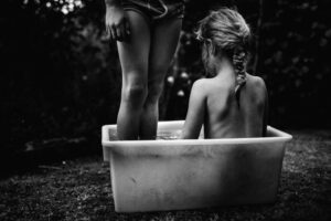 A girl sitting in the tub with another girl standing next to her.