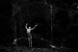 A man standing in the woods with his arms raised.