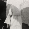 A woman in white holding an umbrella over her head.