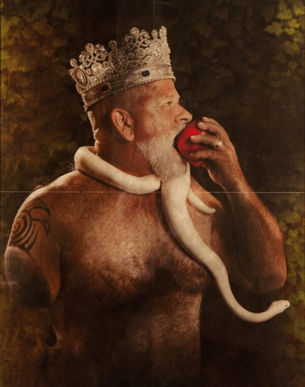 A man with a beard and a crown eating an apple.