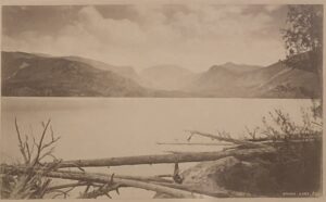 A black and white photo of a lake with mountains in the background.