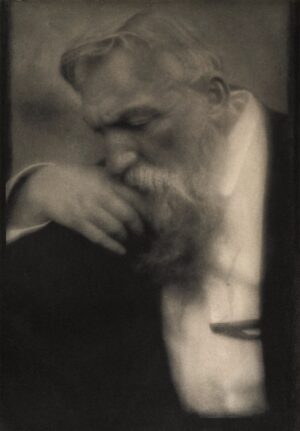 A man with beard and mustache leaning on his hand.