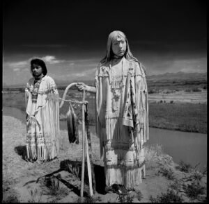 Two women in native dress standing next to a body of water.