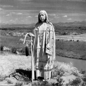 A native american standing in the desert with his staff.