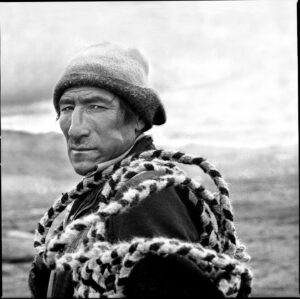 A man in a hat and coat standing on the beach.