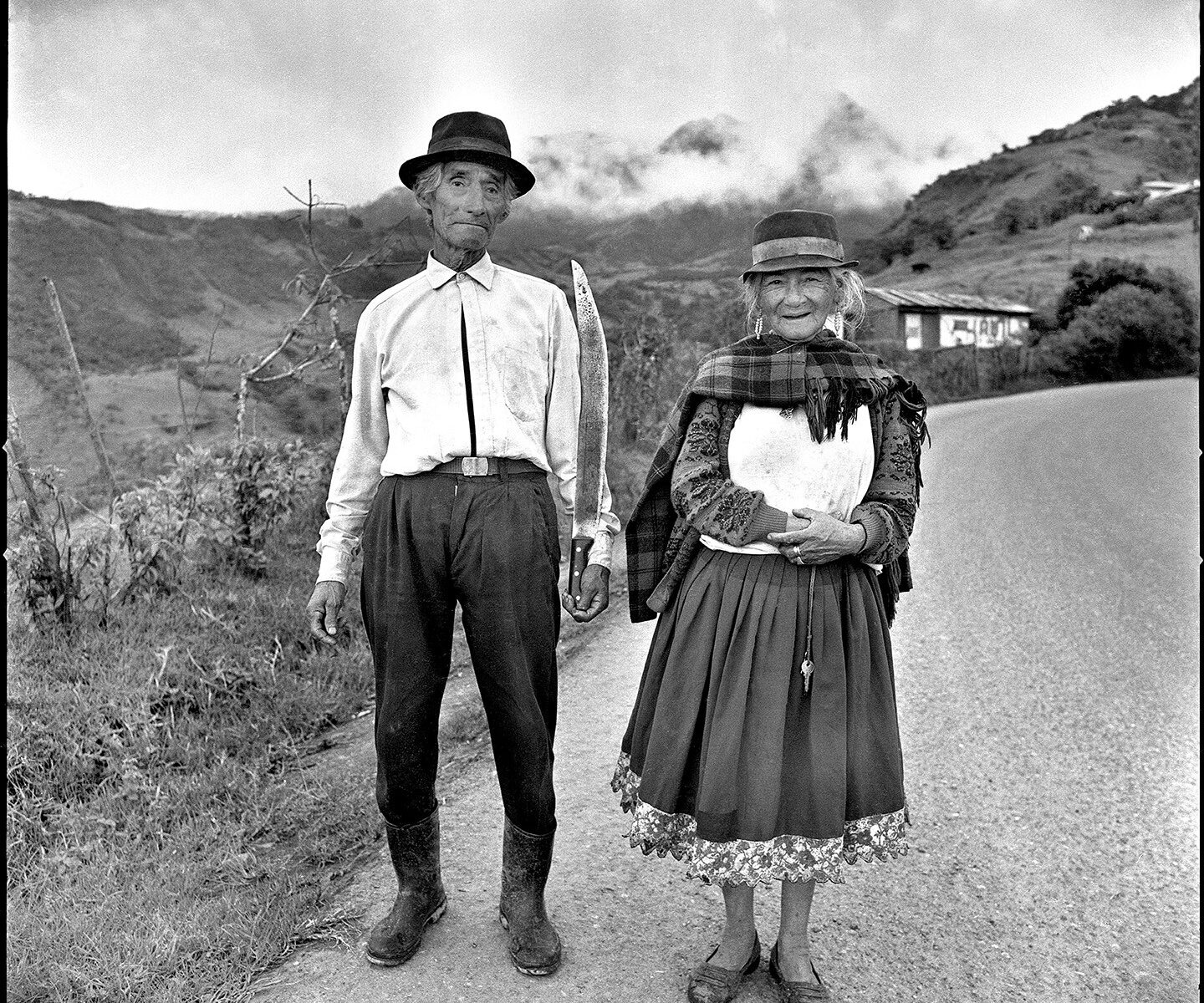 Elderly couple in traditional clothing, holding tools.