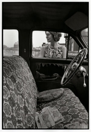 A woman sitting in the driver 's seat of an old car.