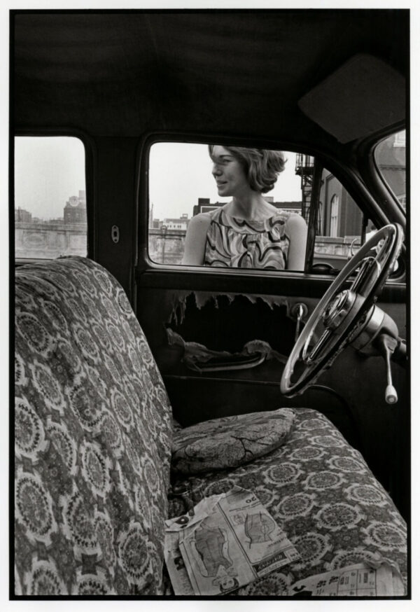 A woman sitting in the driver 's seat of an old car.