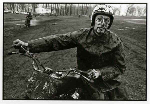 A man riding on the back of a motorcycle covered in mud.