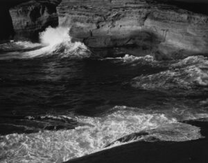 A black and white photo of waves crashing on the beach.