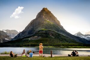 A group of people sitting on the grass near water.