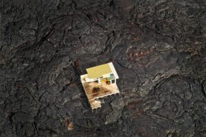 A small yellow house sitting on top of a lava field.