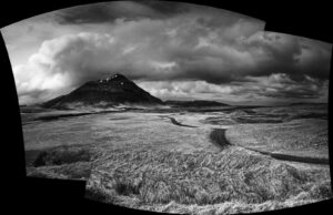 A black and white photo of a field with mountains in the background.