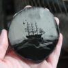 A hand holding a piece of glass with a picture of a ship on it.