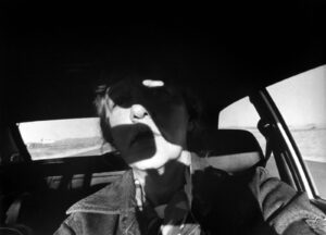 A man with his face covered by the hood of a car.