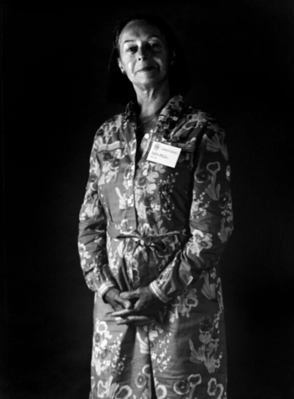 A woman in floral dress holding a cane.