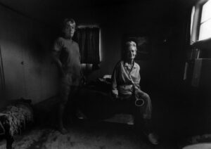 Two people sitting in a room with one standing and the other sitting on a bench.