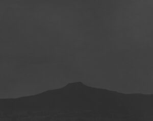 A dark sky with some clouds and a mountain