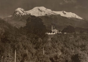A church in the middle of a forest with mountains behind it.