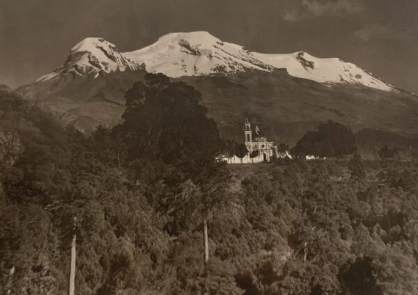 A church in the middle of a forest with mountains behind it.
