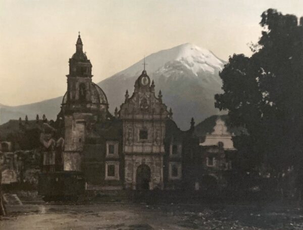 A black and white photo of an old building with a mountain in the background.