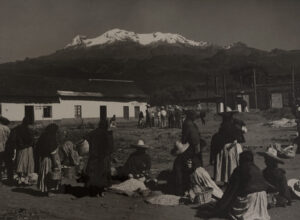 A group of people sitting on the ground near a mountain.
