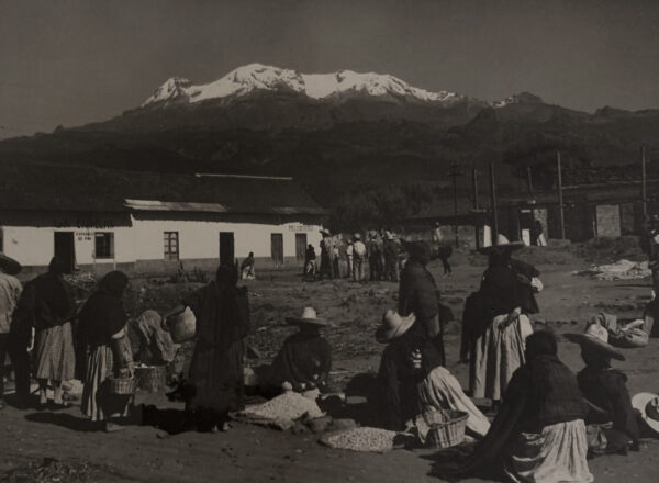 A group of people sitting on the ground near a mountain.