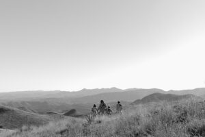 Three people riding bikes in a field with mountains behind them.