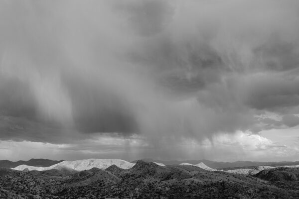 A black and white photo of the sky with rain coming in.
