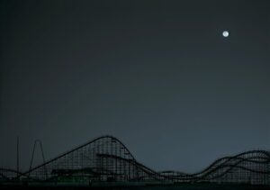 A roller coaster is shown at night with the moon in the background.