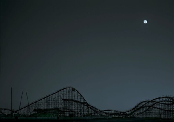 A roller coaster is shown at night with the moon in the background.