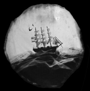 A ship is in the water and there are birds flying above it.
