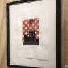 A framed picture of a woman sitting on a chair.