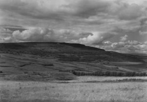 A black and white photo of a field with clouds in the background.