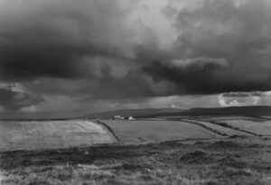 A black and white photo of a field with storm clouds in the background.