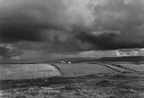 A black and white photo of a field with storm clouds in the background.
