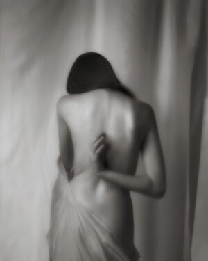 A woman standing in front of a curtain with her back turned.