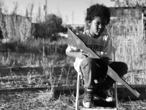 A young boy sitting on top of a chair holding a skateboard.