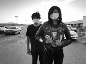 Two people standing in a parking lot wearing masks.