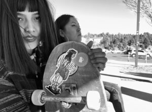 A woman holding up a skateboard with an indian sticker on it.