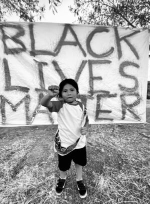 A young boy holding up his fist in front of a black lives matter sign.
