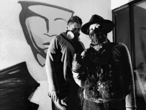 Two men in masks standing next to a wall.