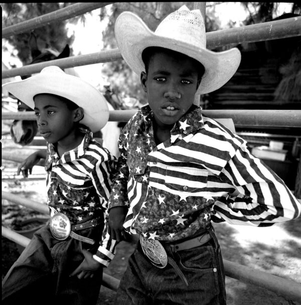 Two young cowboys in cowboy hats and american flag shirts.