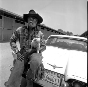 A man with a dog sitting on the hood of his car.