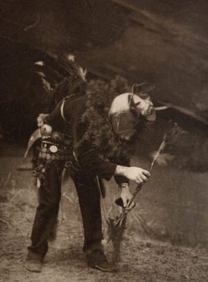 A man in costume holding a stick and wearing a hat.