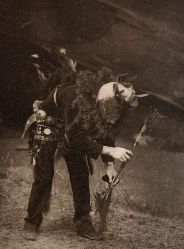 A man in costume holding a stick and wearing a hat.