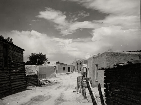 A dirt road with buildings and fences on it