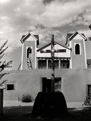 A black and white photo of a church with a cross in front.