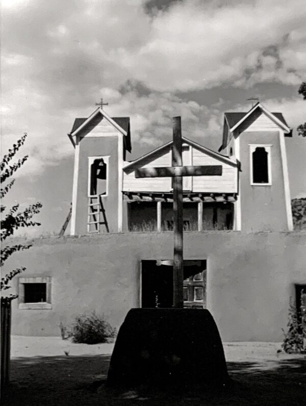 A black and white photo of a church with a cross in front.