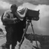 A man standing on top of a hill with an old camera.